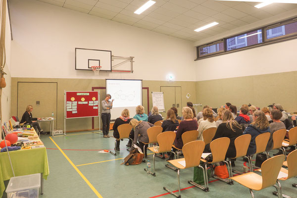 Lehrkräfte lauschen dem Vortrag, auf Tischen liegen Materialien (zum Beispiel ein Blindenfußball und Kapselohrschützer)